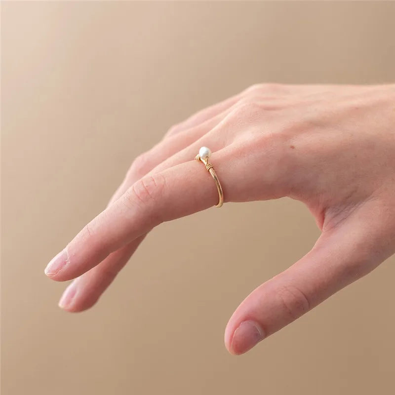 Hand wearing a gold ring with a small pearl on a beige background