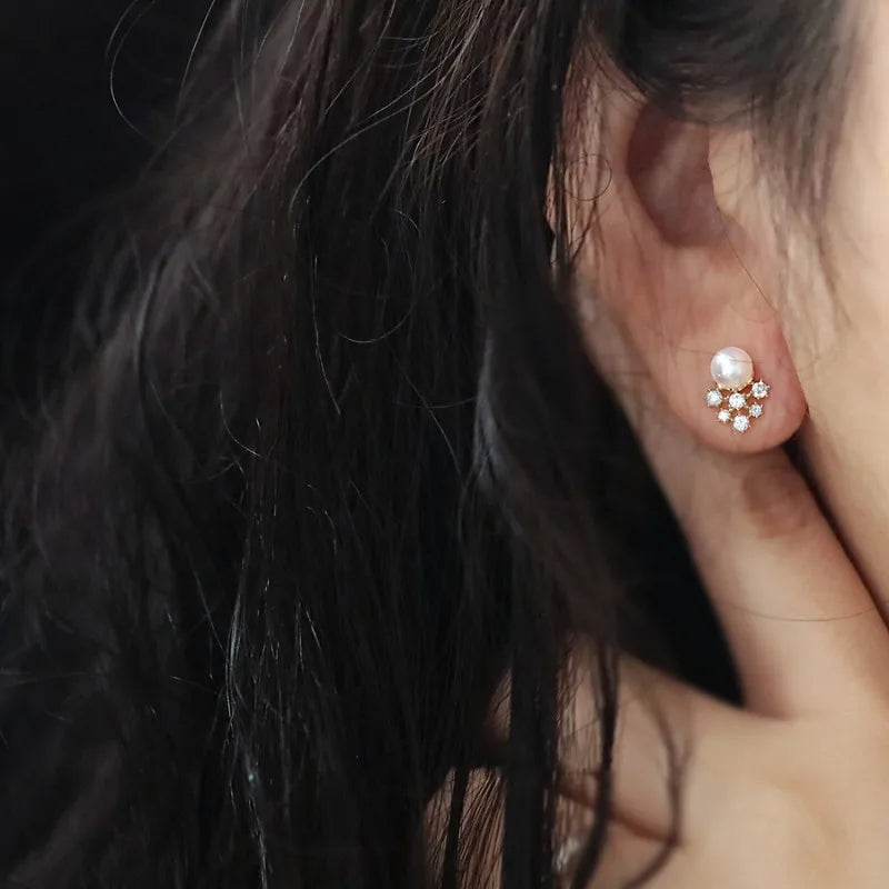 Close-up of an ear wearing a pearl earring with small crystals, against a dark background.