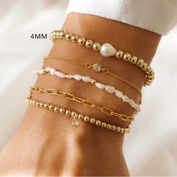 Stack of gold and pearl bracelets on a wrist with 'OriginaIngenu' branding.