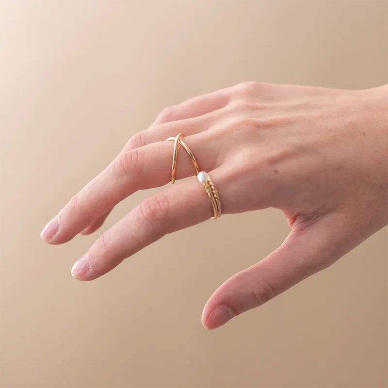 Hand wearing a gold ring with a pearl on a beige background