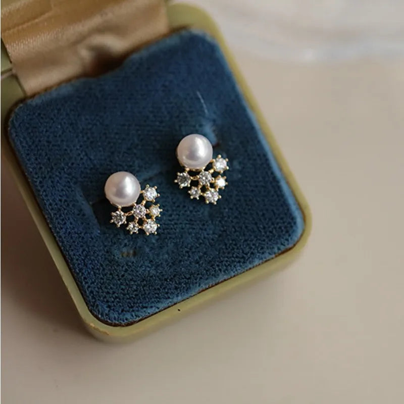 Pearl earrings with star-shaped diamond accents on a blue cushion in a jewelry box.