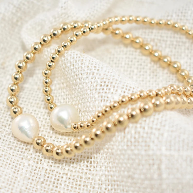Gold beaded necklace with pearls on a textured white background
