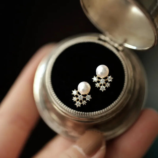 Pearl earrings with star-shaped diamond accents in a silver case held by a hand.