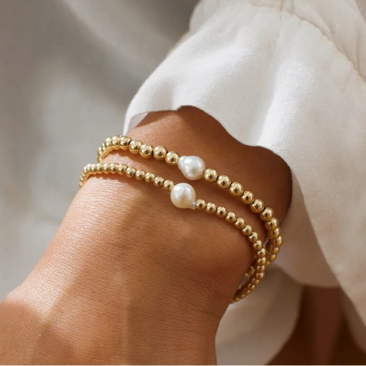 Gold beaded bracelet with pearl accents on a wrist against a neutral background