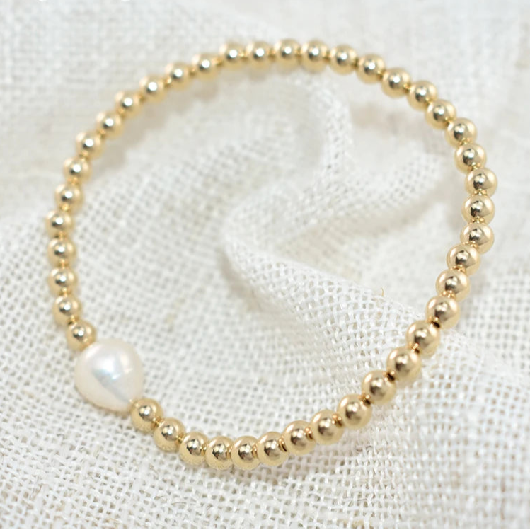 Gold beaded bracelet with a pearl on a textured white background