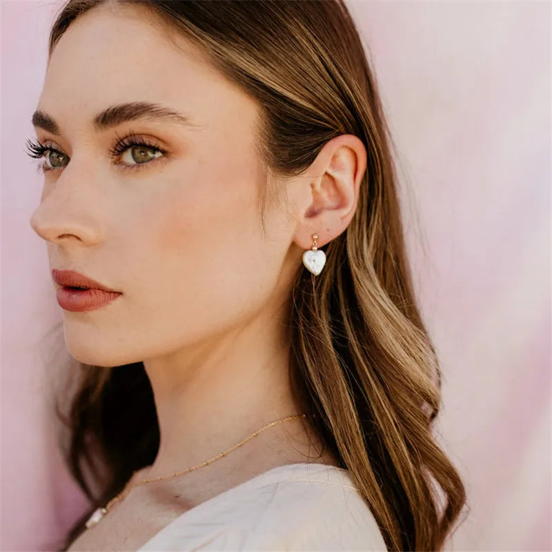 Close-up of a woman wearing heart-shaped earrings with a soft pink background