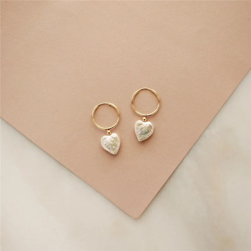 Gold heart-shaped earrings on a beige background